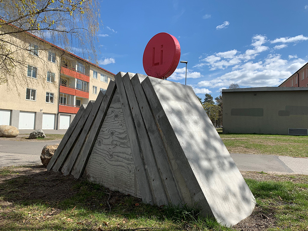Konst med triangelformad betong ioch en röd rund knapp med bokstäverna Li