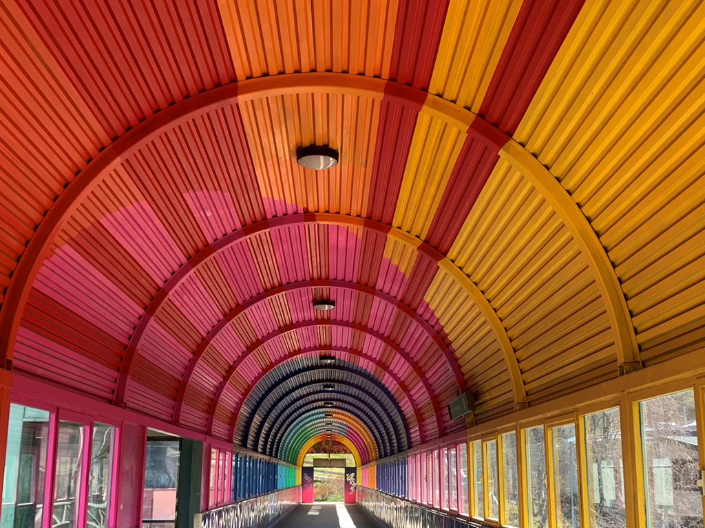 Tunnel med ttak i starka regnbågsfärger som gult, orange, rosa, lila och fönster på sidorna.