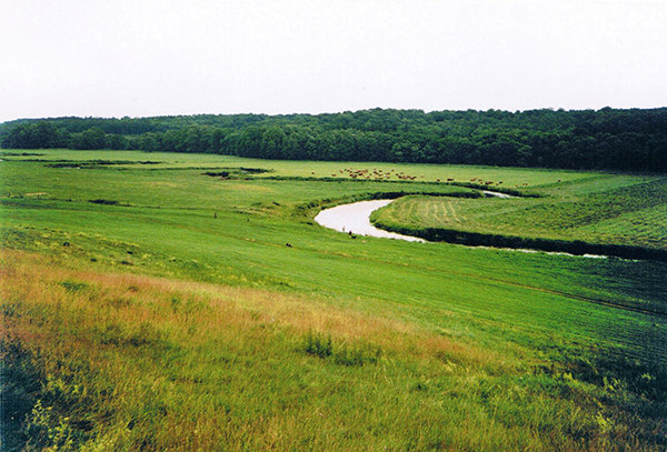 En flod som slingrar sig fram, med åkermark på båda sidor.