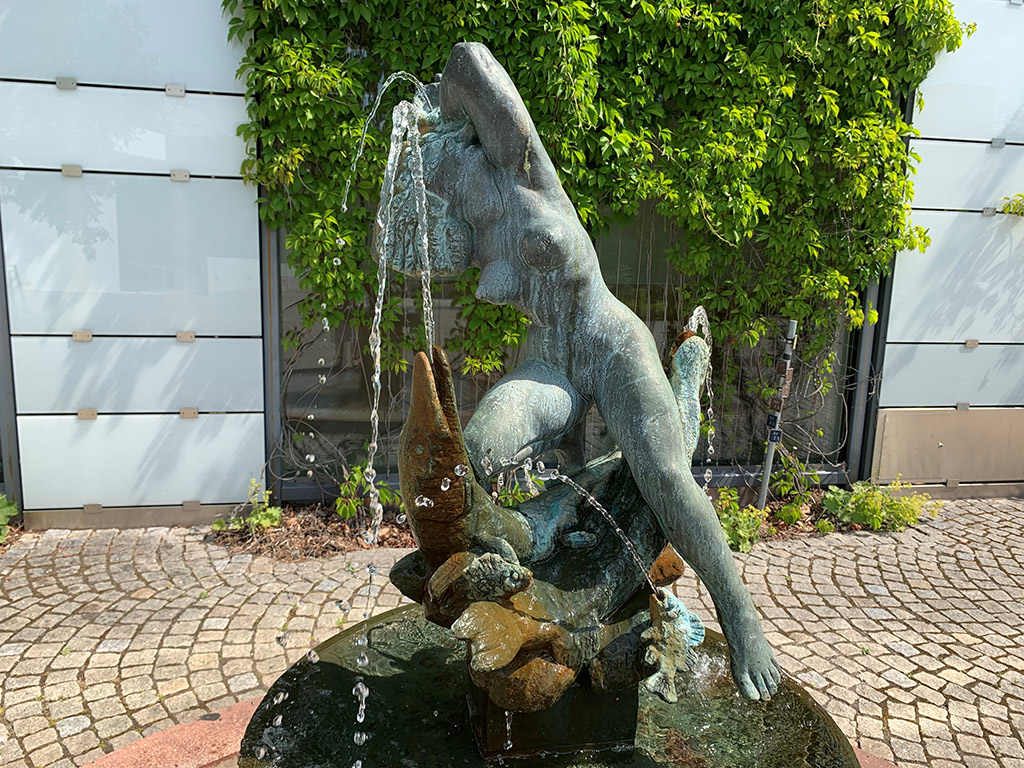 Bronsskulptur av en naken kvinna på fisk i en fontän