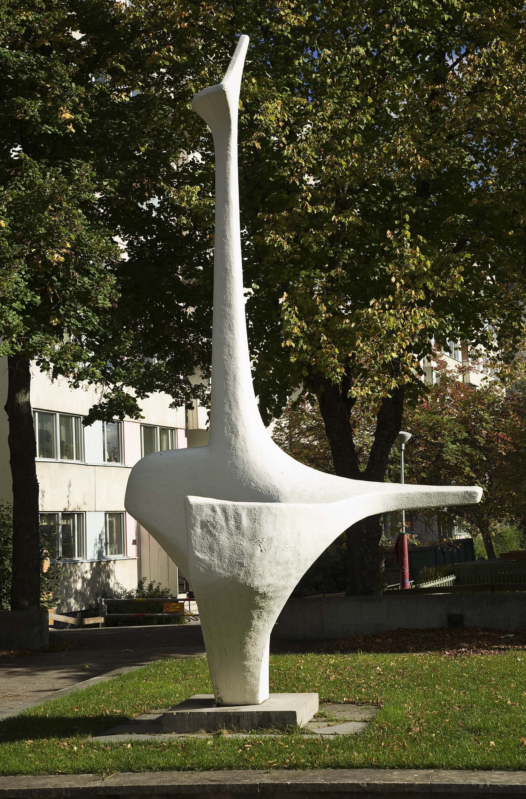 En vit abstrakt skulptur med lång hals som står på en gräsmatta.