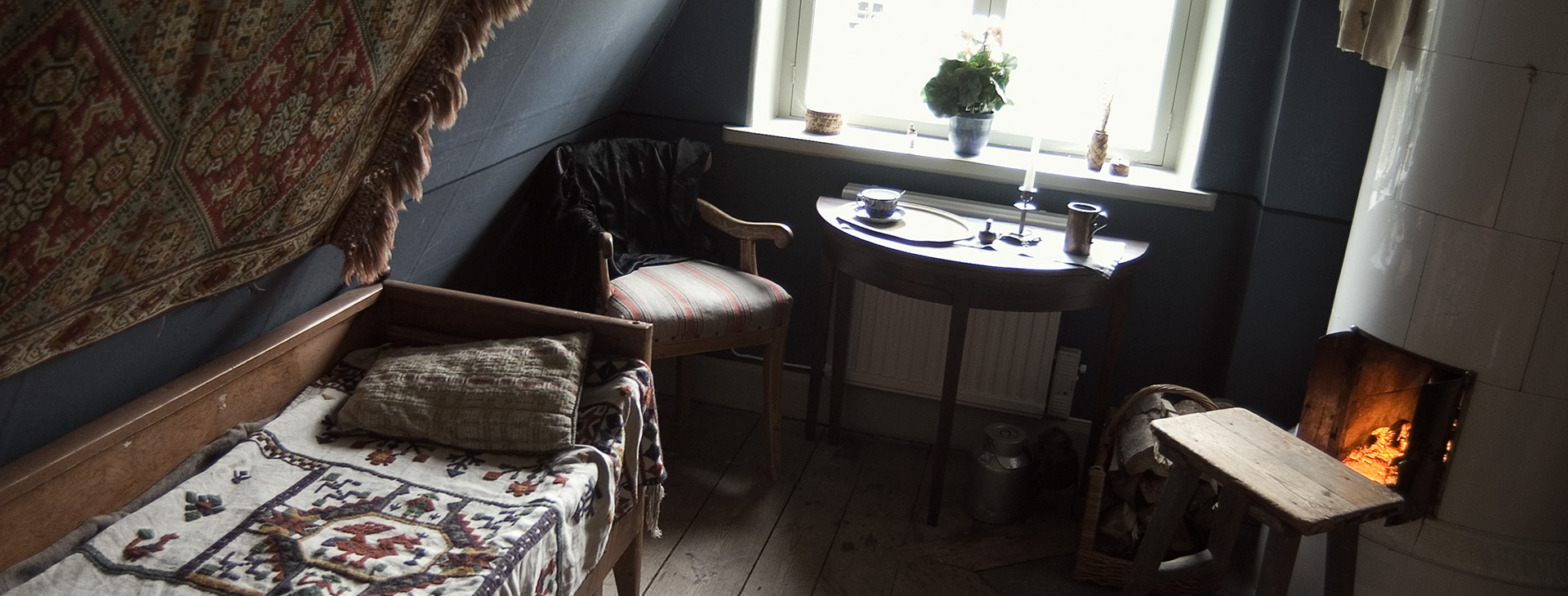 Ett rum med säng, stol, bord och en kamin som det brinner i.