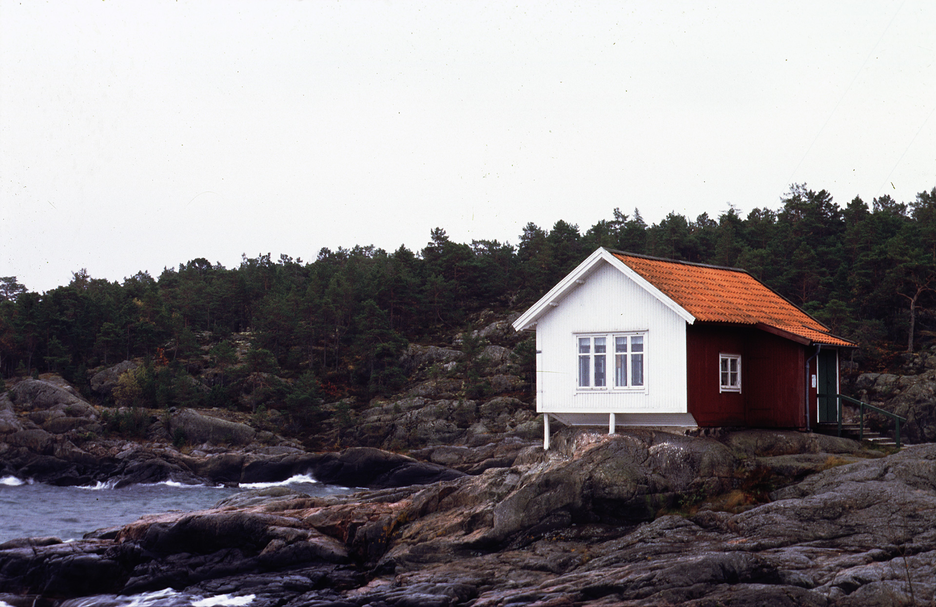 Ett litet hus som står på klipporna. Det är nära havet.