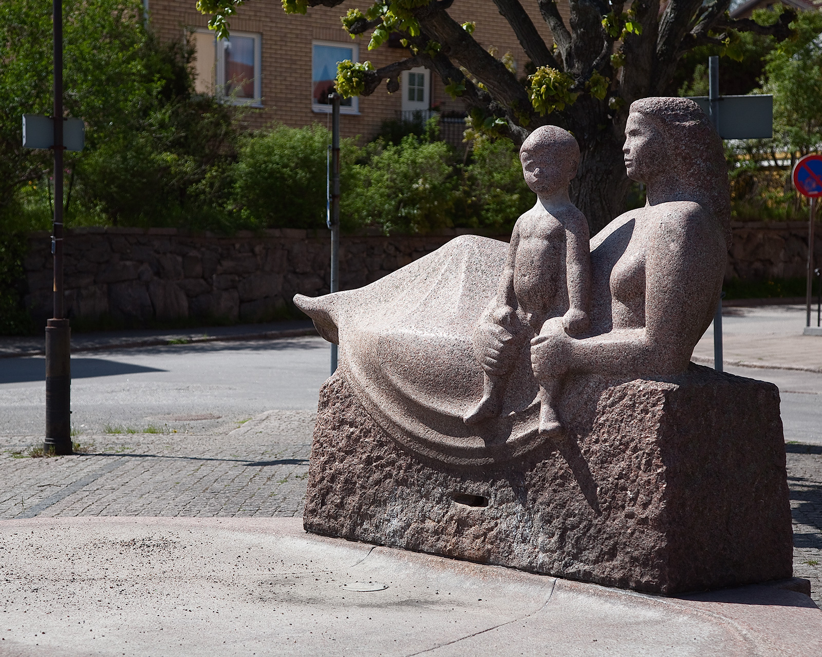 En skulptur av sten av en kvinna som halvligger med en pojke framför sig. 