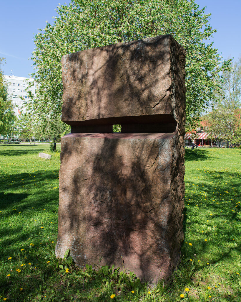 En rektangulär sten med ett litet hål i som står på grönt gräs med ett grönskande träd bakom.