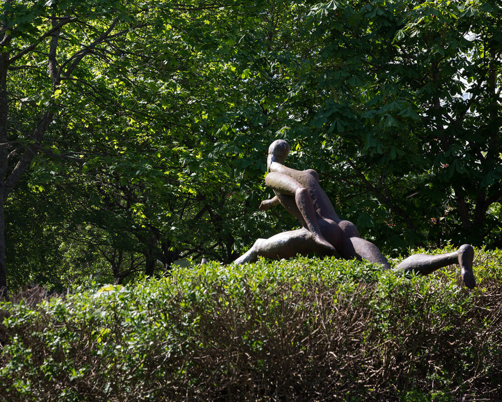 En skulptur, som liknar en häcklöpare, tar ett hopp över en grönskande häck.