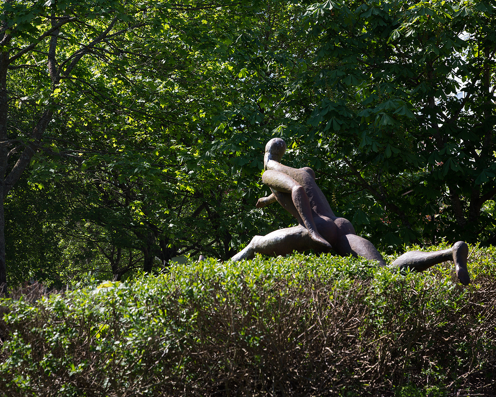 En skulptur, som liknar en häcklöpare, tar ett hopp över en grönskande häck.