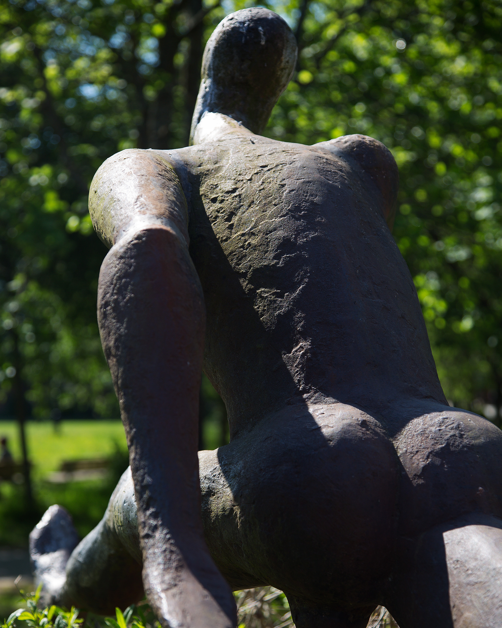 Ryggen på en skulptur av en naken man. Grönska i bakgrunden