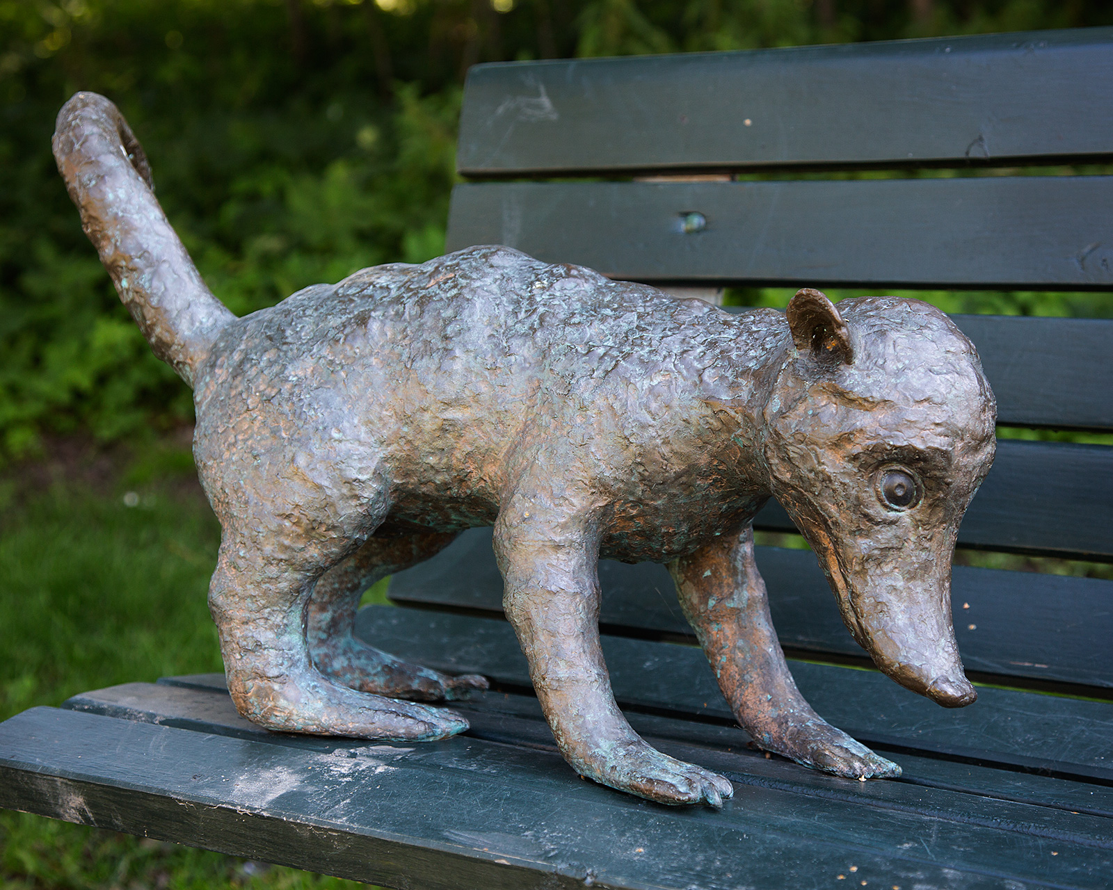 En näsbjörn gjord av sten står på en parkbänk.