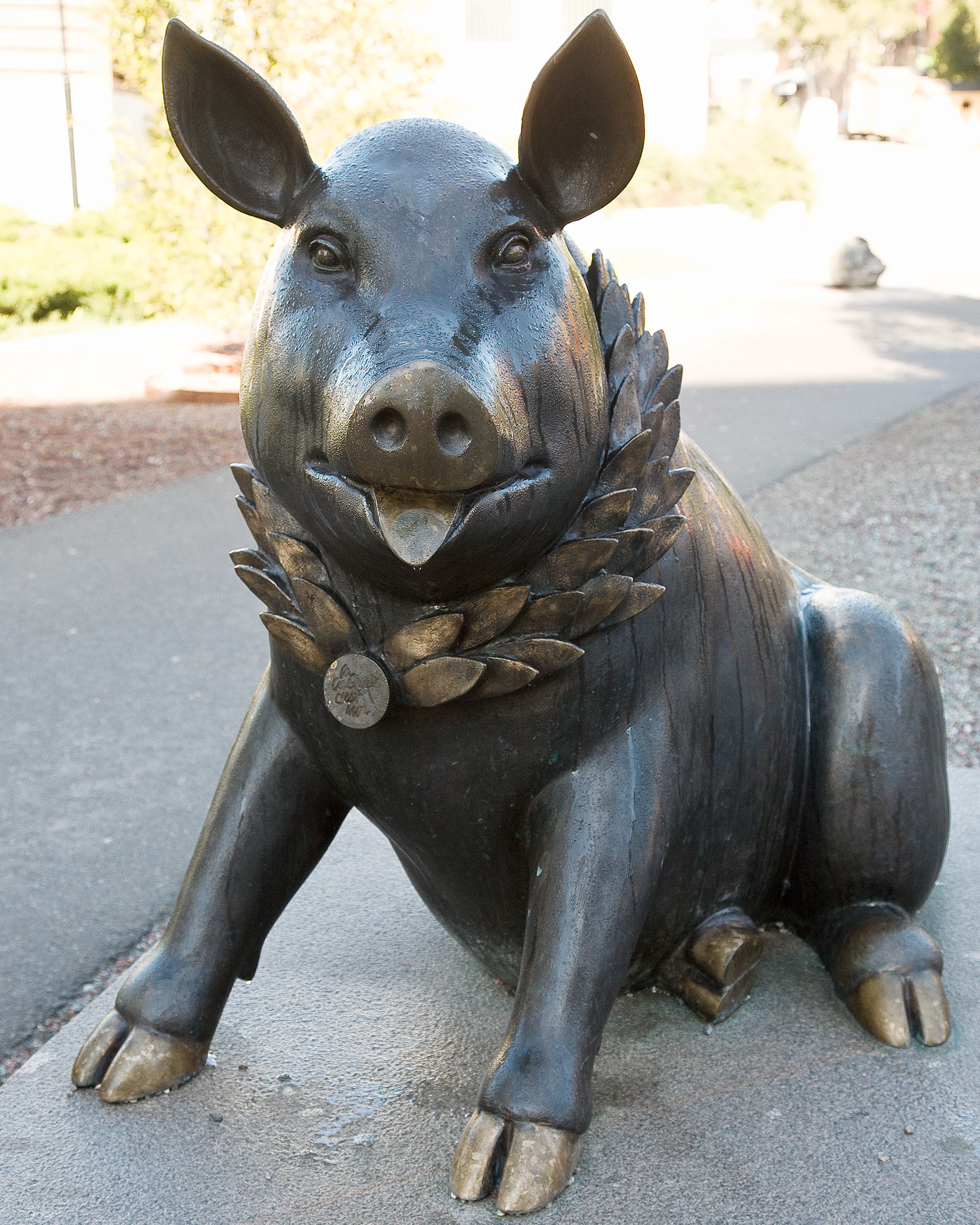 En skulptur av en gris i brons sitter på asfalten och ler.