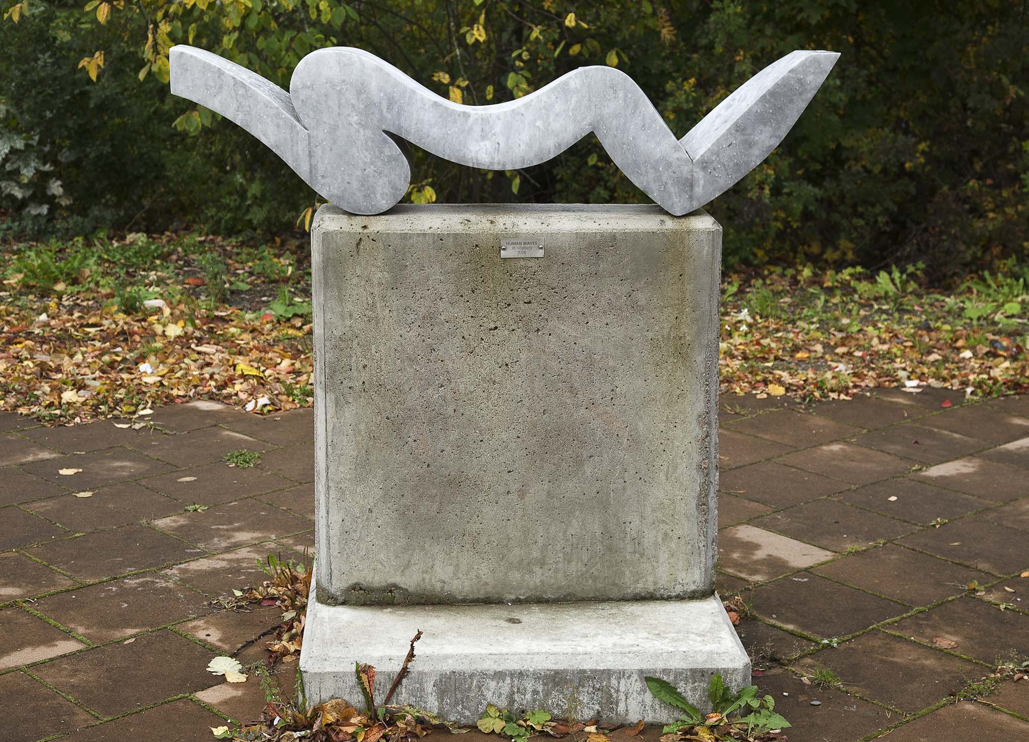 En vågformad skulptur på en kvadratisk sockel av grå sten.
