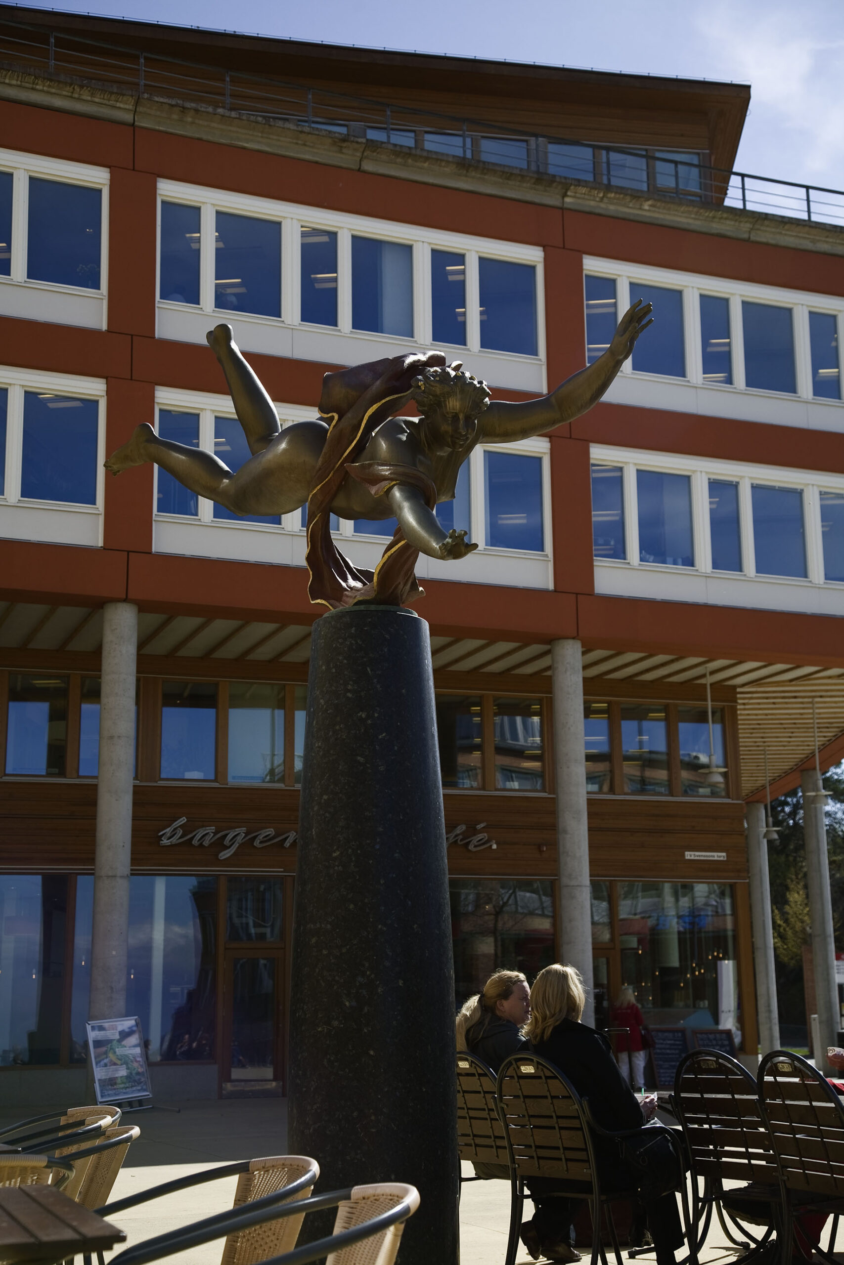 En skulptur av flygande flicka med ett skynke på ryggen uppe på en svart sockel.