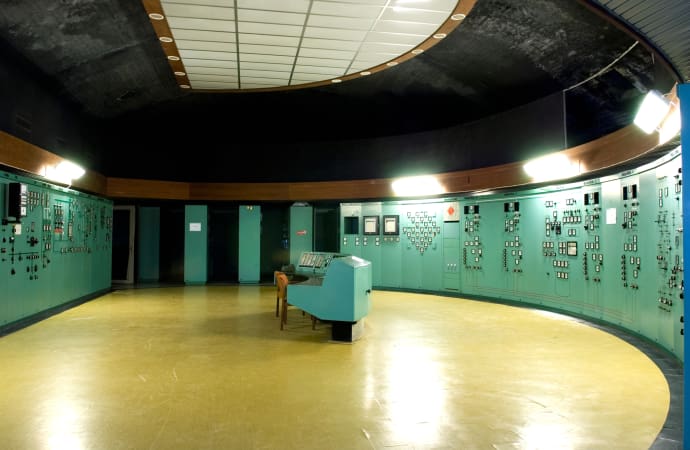 Ett halvcirkelformat rum som har kontrollpaneler på väggarna. I mitten står en apparat.