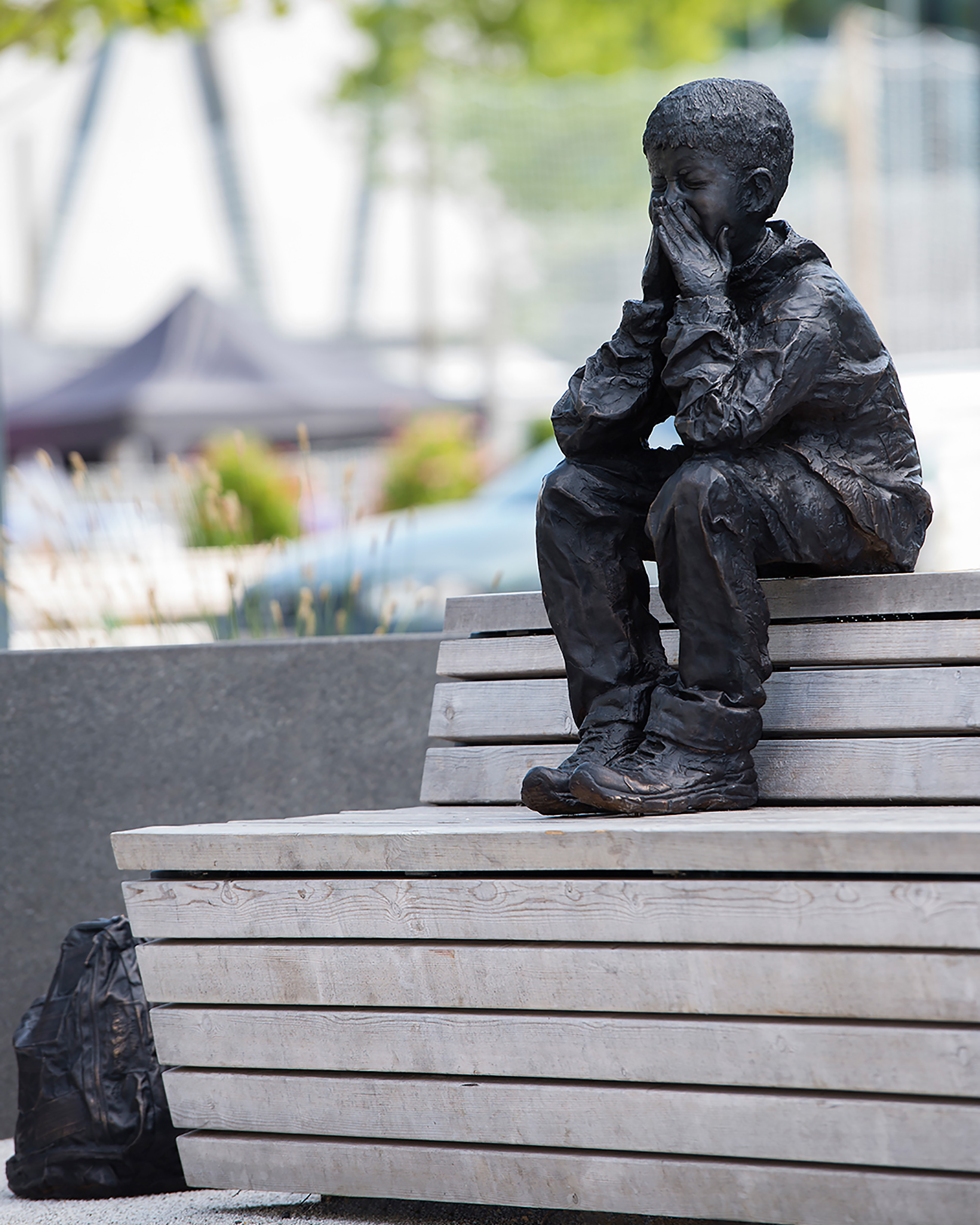 En pojke gjord av brons som sitter på en parkbänk.
