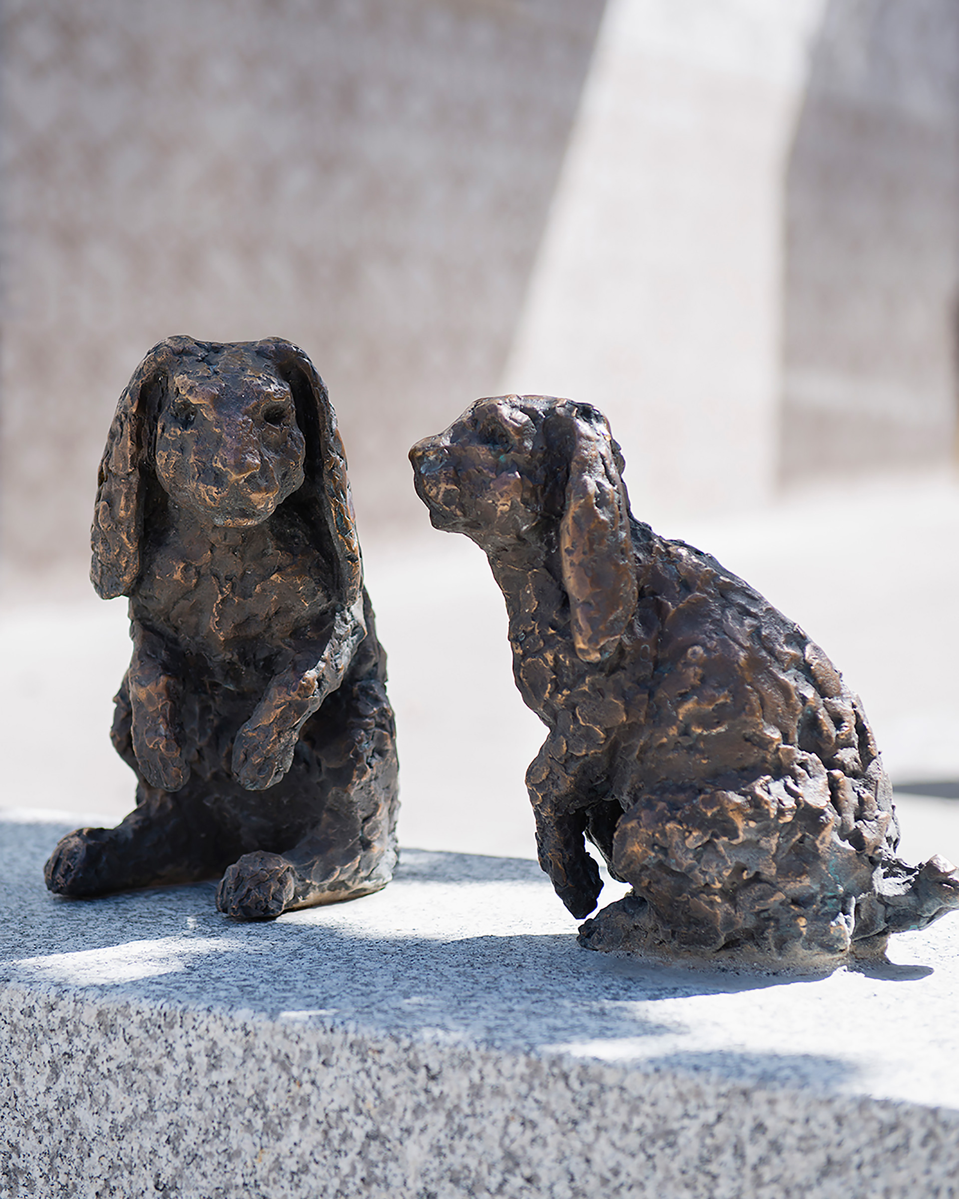 Skulptur med två kaniner i brons som sitter på en grå sten.