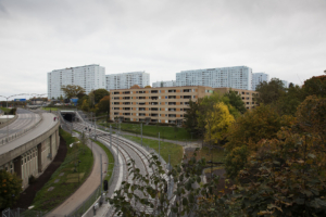 Vy över Hagalunds blåa silhuett, gula lamellhusen på Kyrkbacken, och tvärbanespåren i förgrunden.