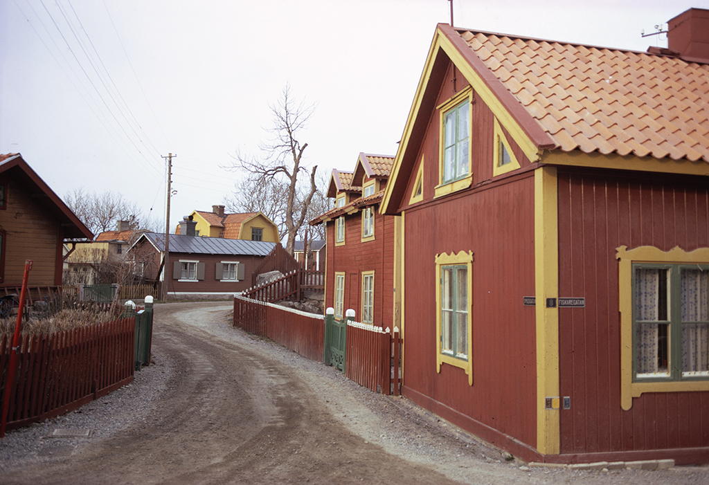 En liten gata gjord av grus. Det står små hus längs med gatan.