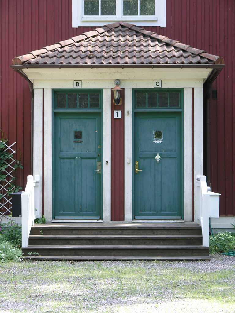 En veranda med två dörrar, en trappa leder upp till dörrarna.