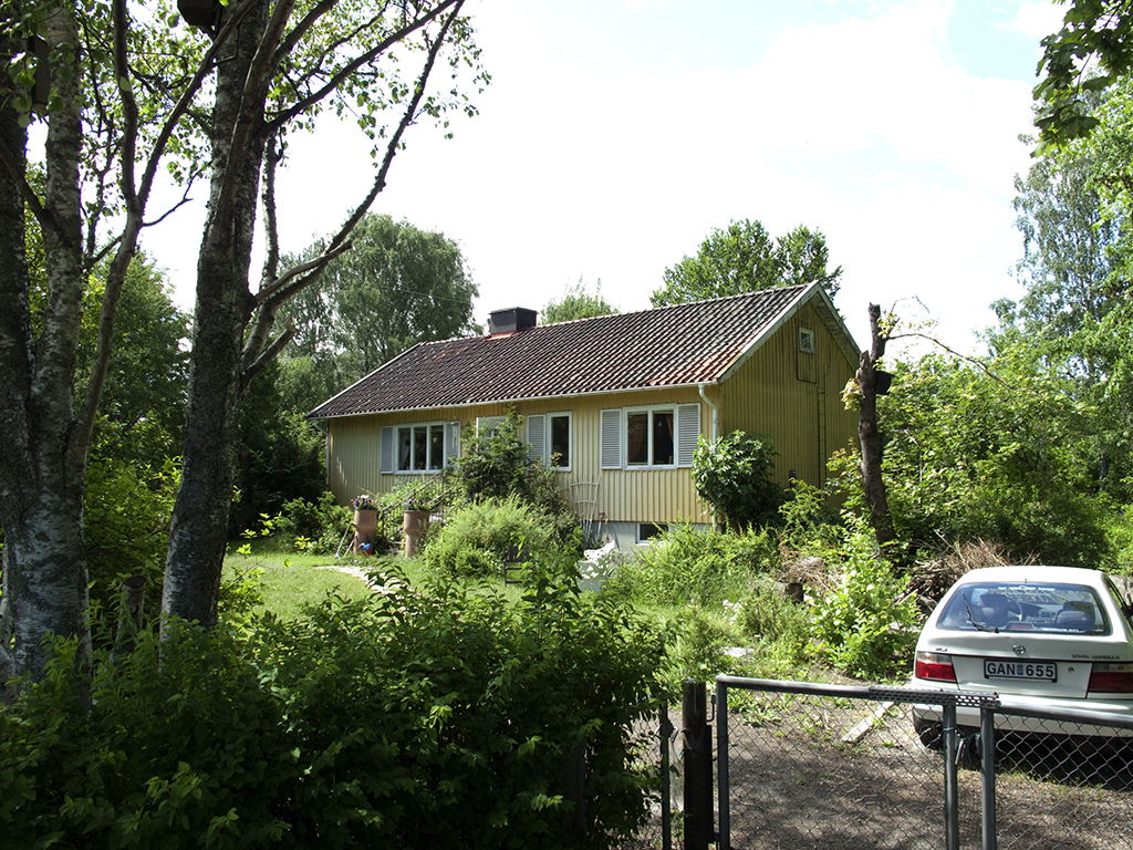 En hus som står på en trädgård, närmast i bild står en bil parkerad.