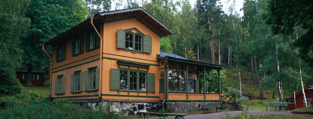 Ett hus med stora fönster, det är skog runt huset.