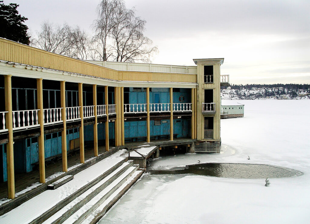 Ett hus som ligger vid vattnet. Det är vinter och ett hål i isen har gjorts. Där i kan man bada.