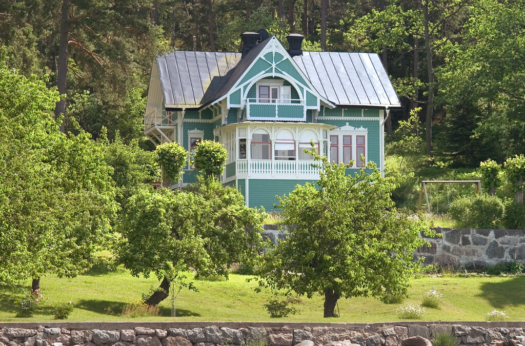 Ett hus som står i en trädgård med träd framför huset. Det är sommar.