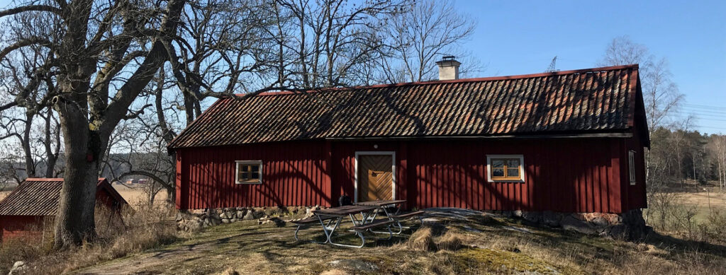 Exteriör av Lundby parstuga. Rödmålad träbyggnad med. Taktegel och murad skorsten.