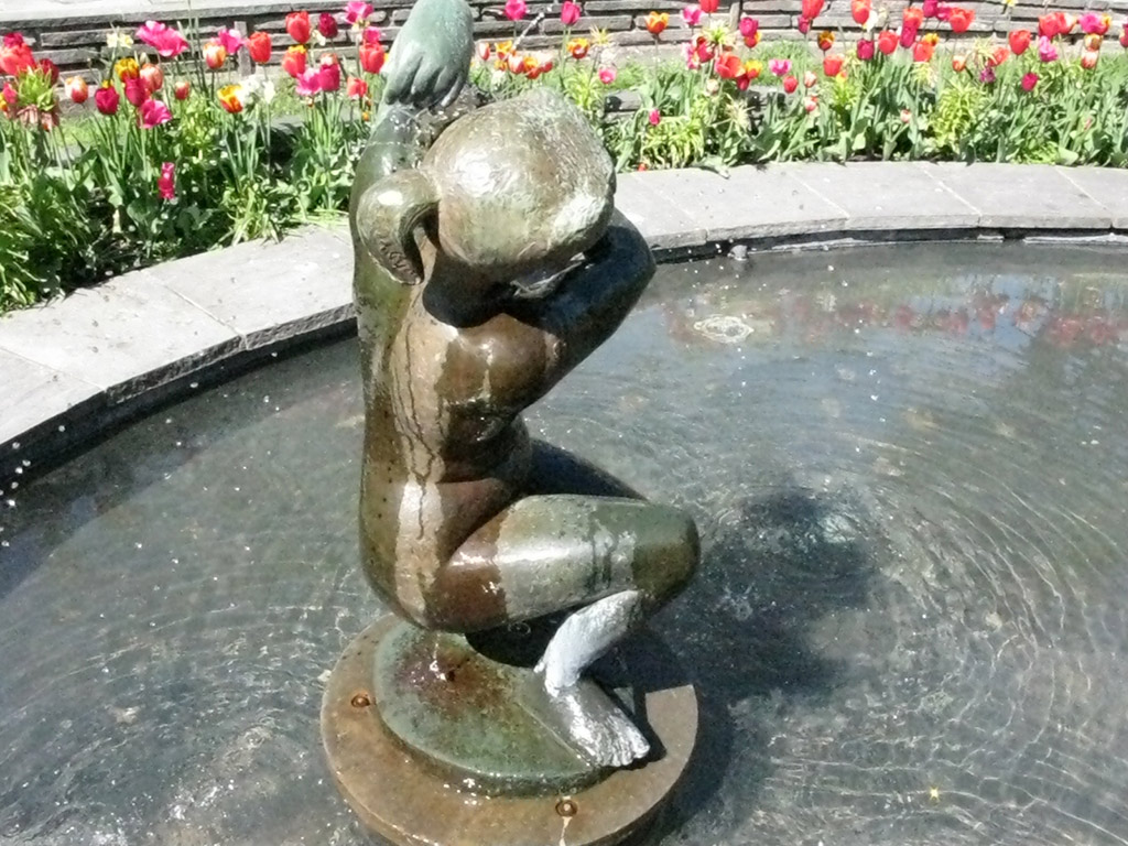 En skulptur av en naken flicka sitter på huk och tvättar sig.