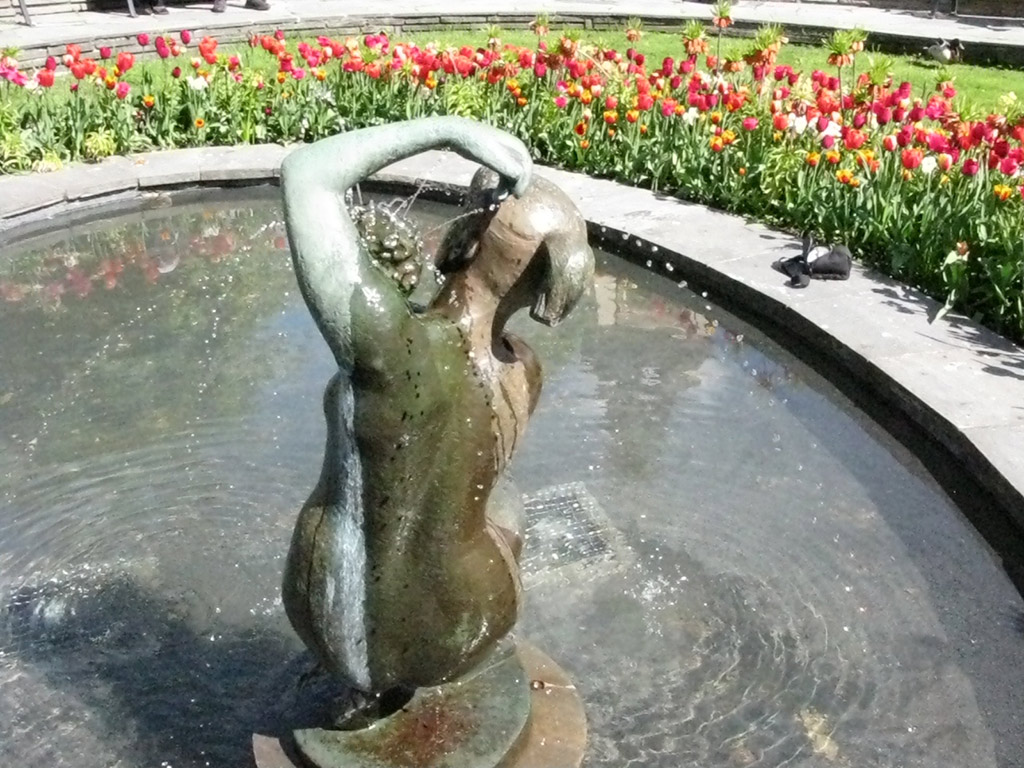 En skulptur av naken flicka sitter på huk och tvättar sig i fontänen.