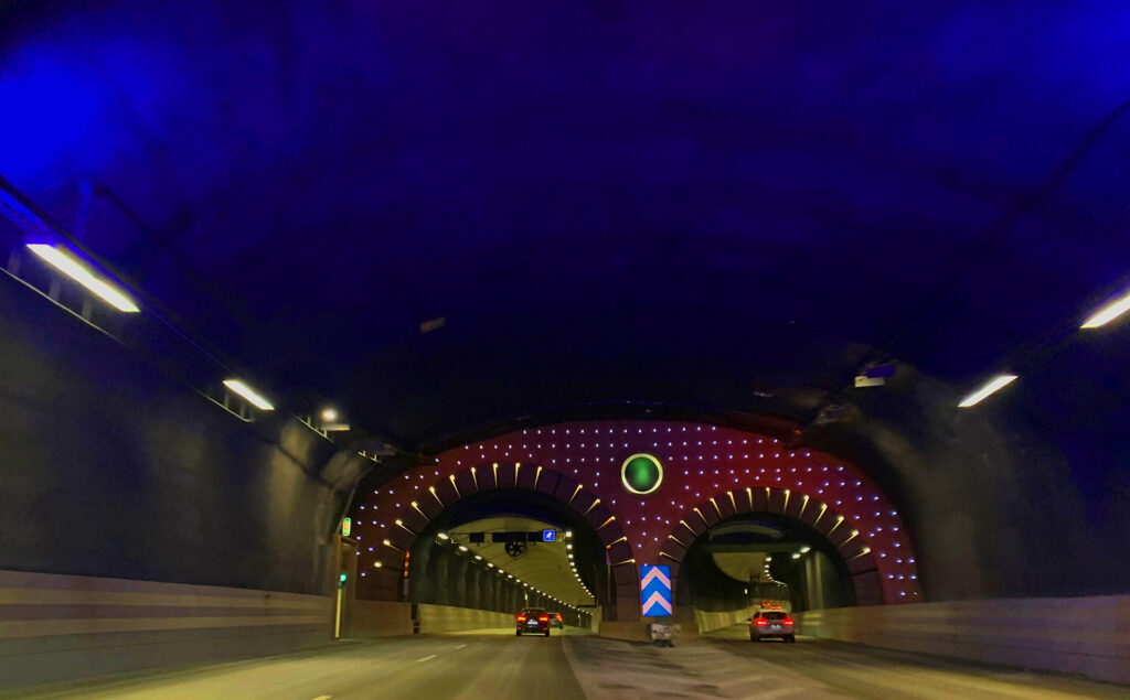 Bild tagen i en tvåfilig biltunnel. Koboltblått tak med randiga valv och lysande ring i mitten. Lysande lampor ovanför valvet.