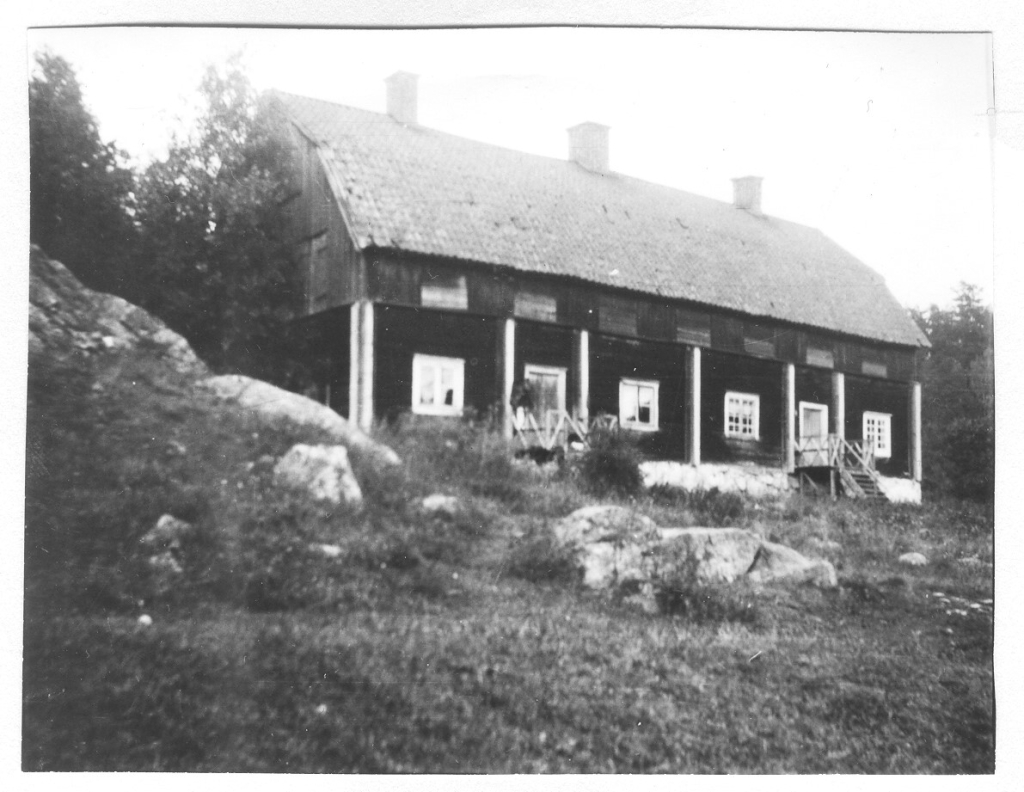 Svartvitt fotografi, stort trähus i skogsbacke.