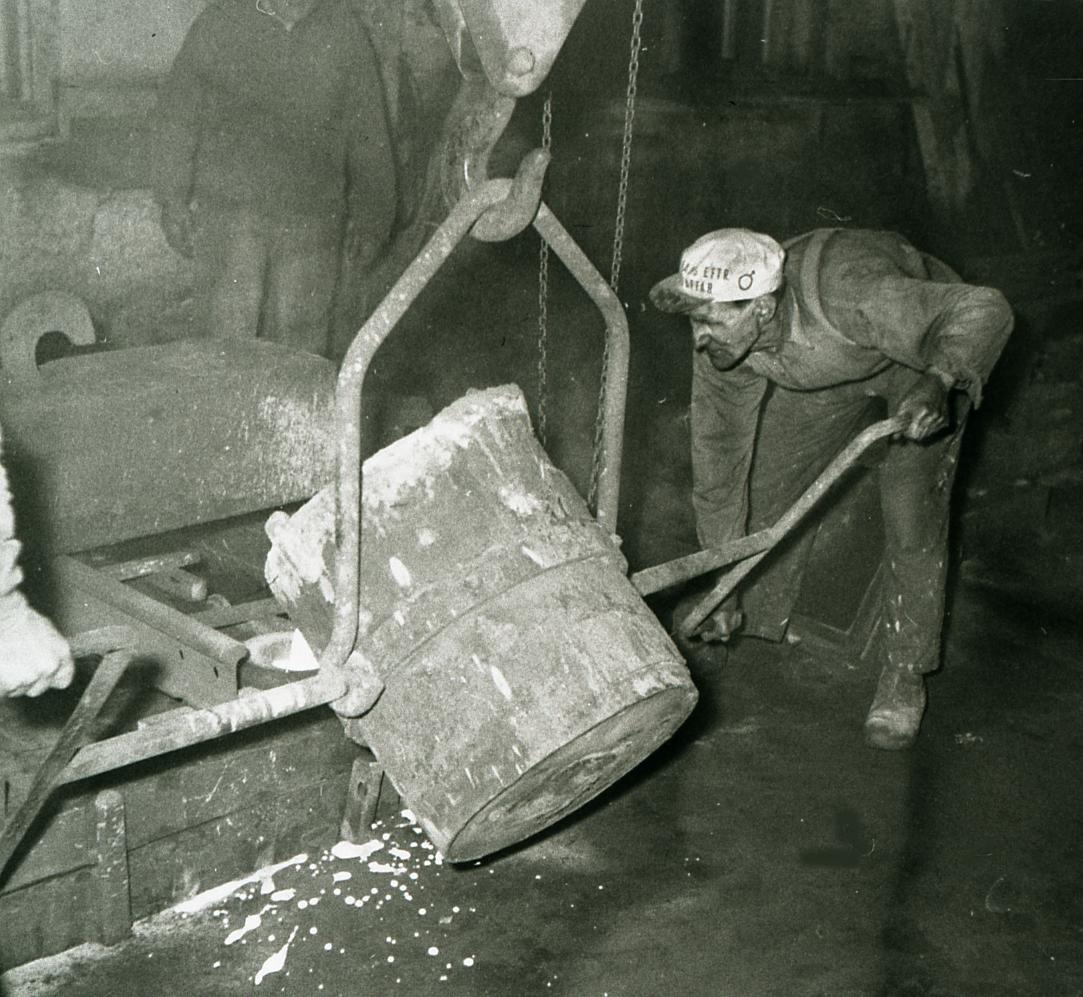 En man med keps böjer sig ner för att välta ut innehållet i en stor behållare.