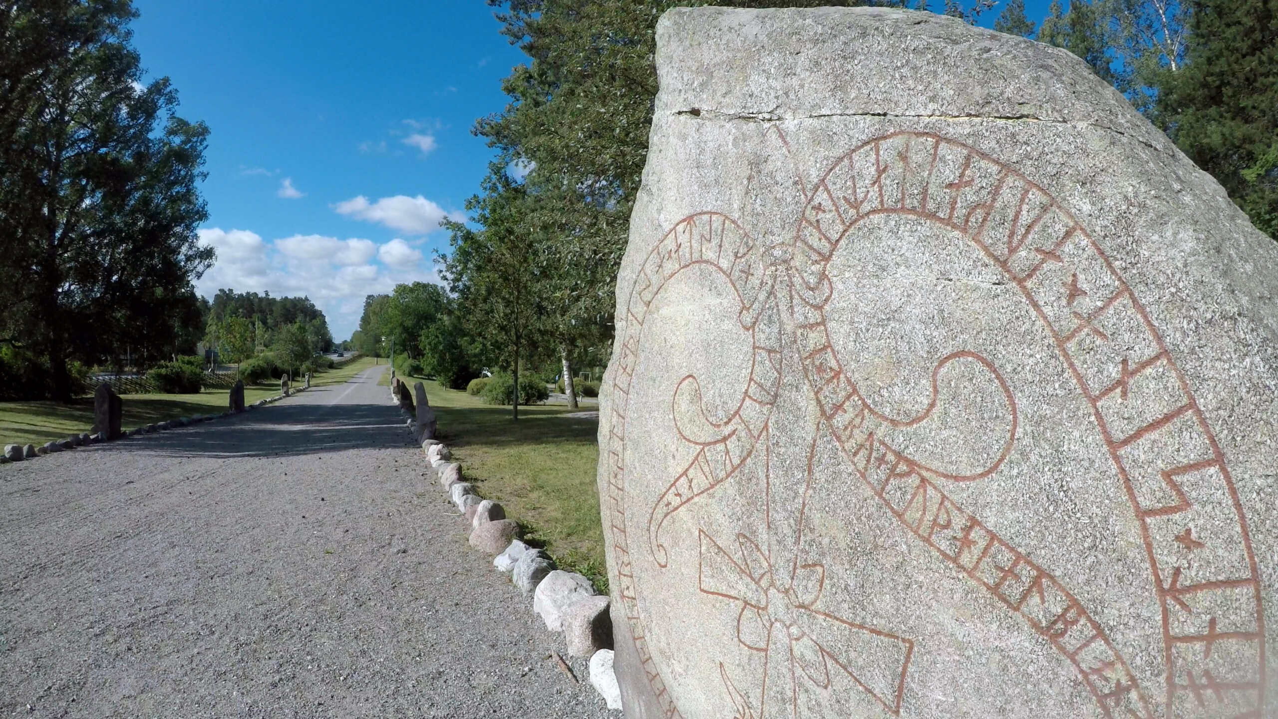 Runsten i förgrunden med en grusväg kantad av stenar i bakgrunden.