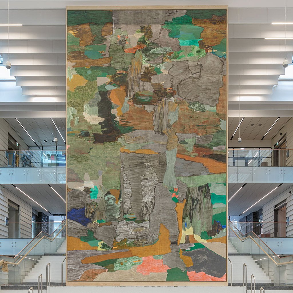 Abstrakt målning med olika färger som grått, grönt, orange, rosa i trapphall. Målningen är hög som tre våningar