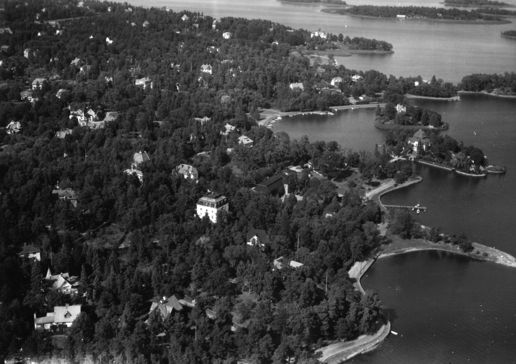 Fågelvy över Djursholm där stora villor sticker upp ur skogen. Kusten är slingrig och några hus ligger på små öar intill kusten.