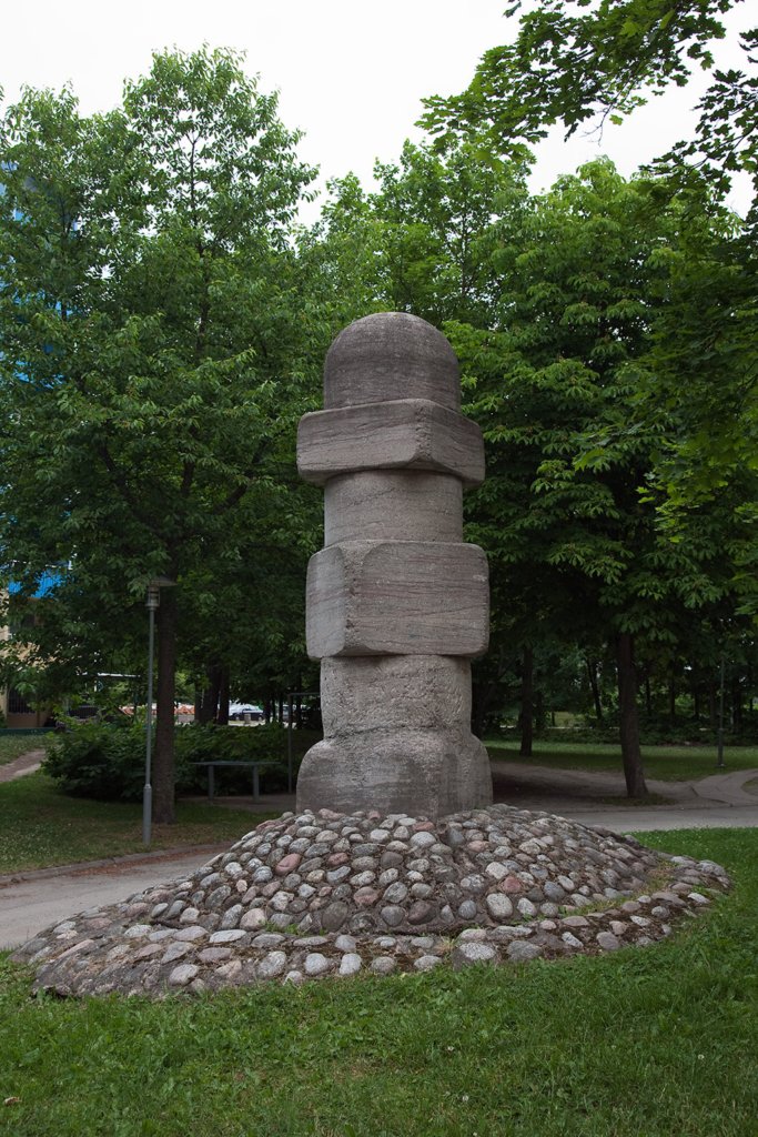 Skulptur av sten med fyrkantiga och runda former som står på gräs. Träd i bakgrunden.