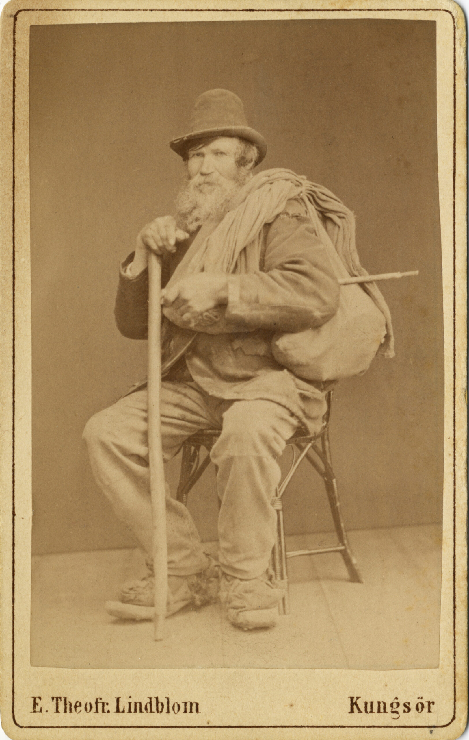 Ett porträttfotografi av man med långt skägg sitter på en stol.