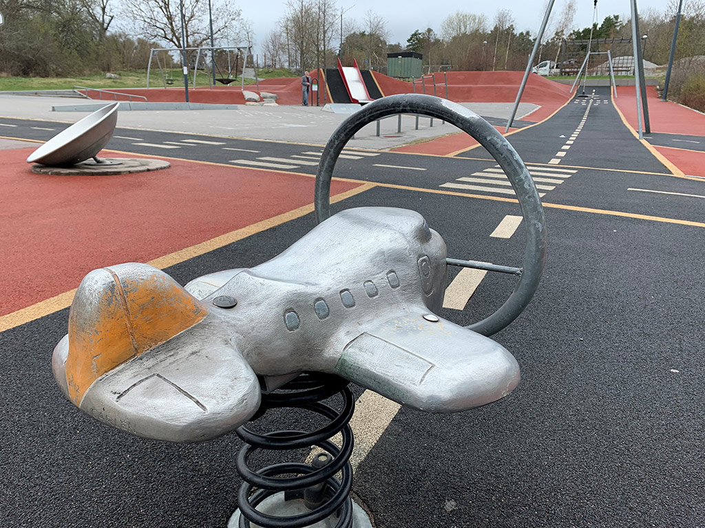 Leksaksflygplan av stål på en lekplats. Svart gulstreckad landningsbana framför.