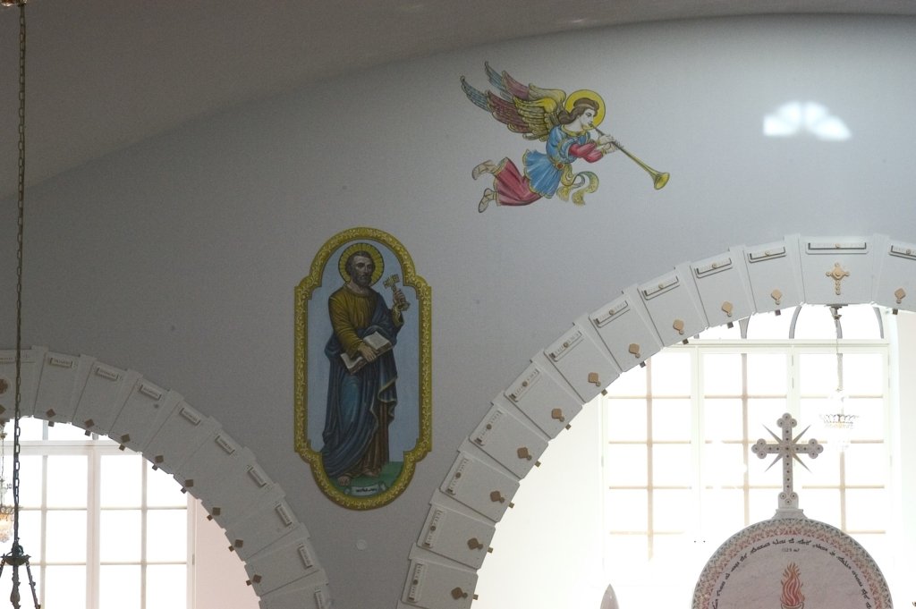 Helgonbilder målade på en vit vägg ovanför ett kyrkfönster.