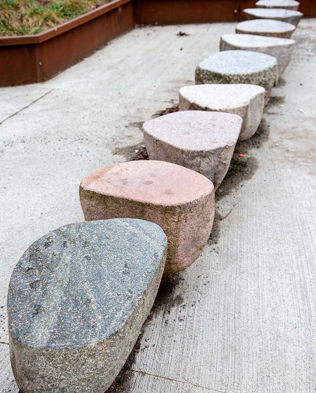 Nio släta stenar i olika nyanser på en rad på grå betong.