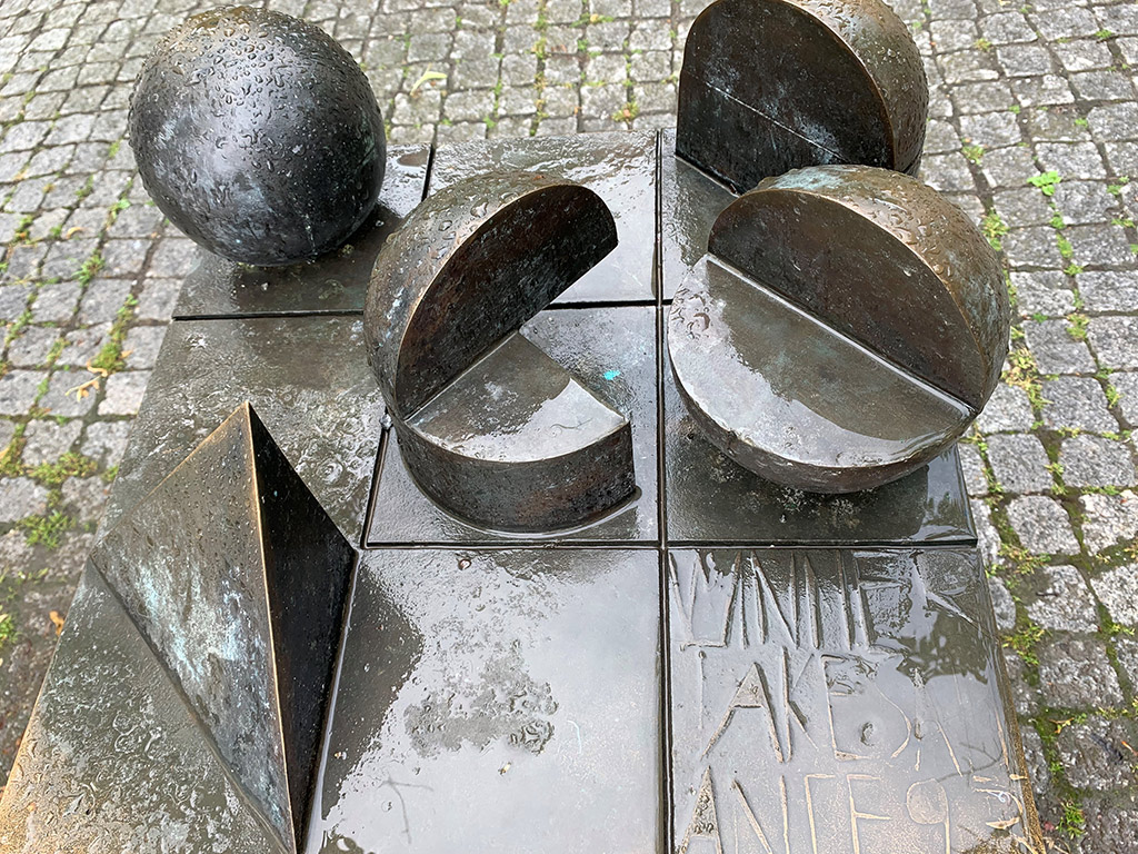 Fem geometriska former, klot, halvklot av brons på en bronsplatta med sex fyrkantiga fält.