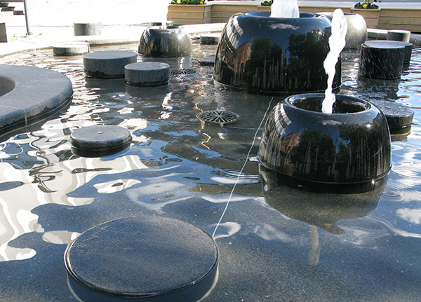 Fontän med svart böj kant, vatten sprutar ur runda former inuti fontänen.