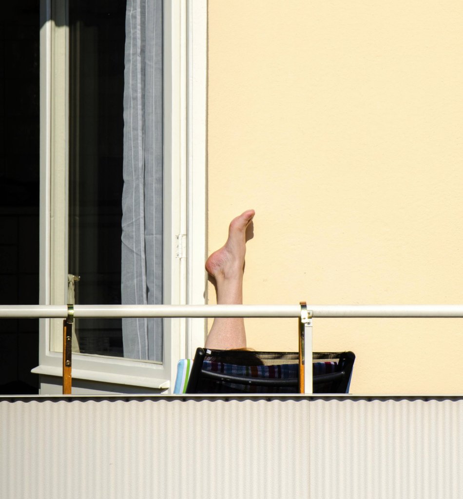 En person ligger i solen på en balkong. Endast en fot sticker upp.