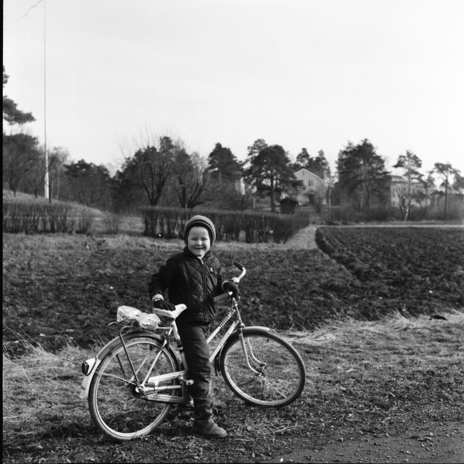 Ett barn står vid sin cykel. I bakgrunden syns en slingrande väg och några hus.