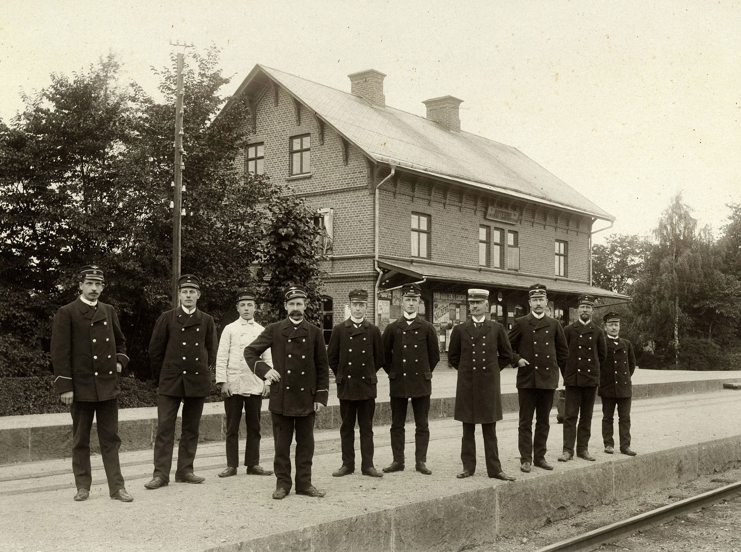 Ett svartvitt fotografi från 1910-talet på personal från Rotebro station som står uppställda framför stationshuset.