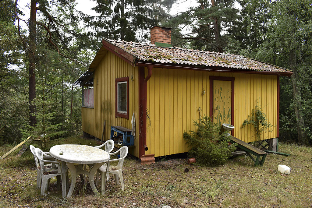 Ett mindre gul stuga i trä med utemöbler framför