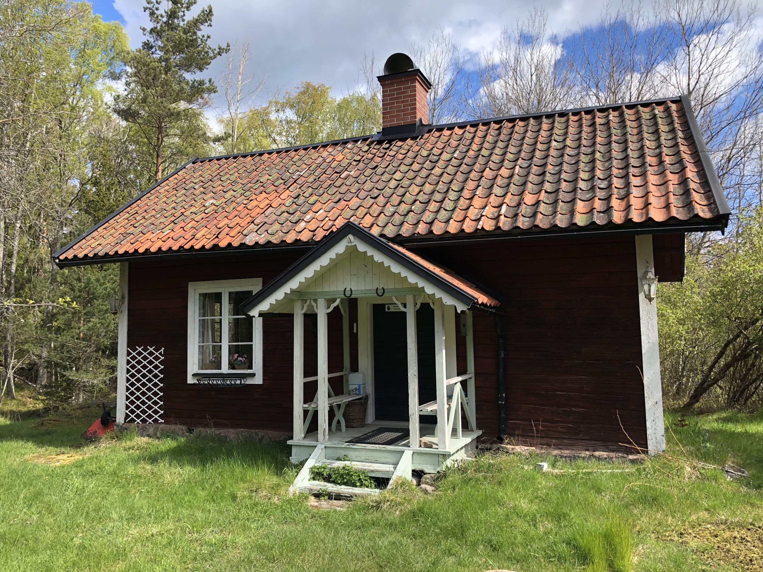 En röd torpstuga med furutkvist och ett enda fönster.