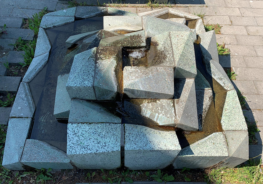 Fyrkantig stenformation med vatten som rinner. Utomhus på stenläggning.