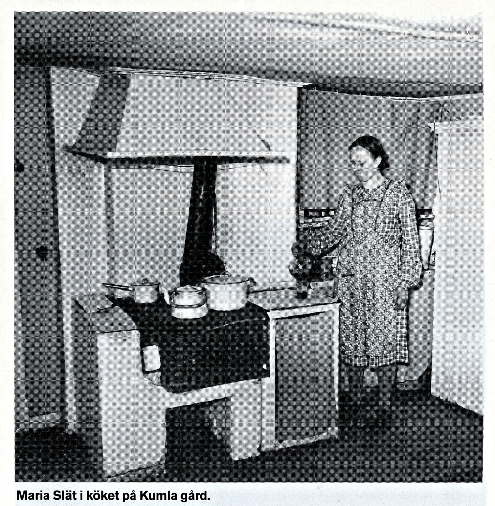 Svartvitt foto av Maria i det ålderdomliga köket med vedspis.