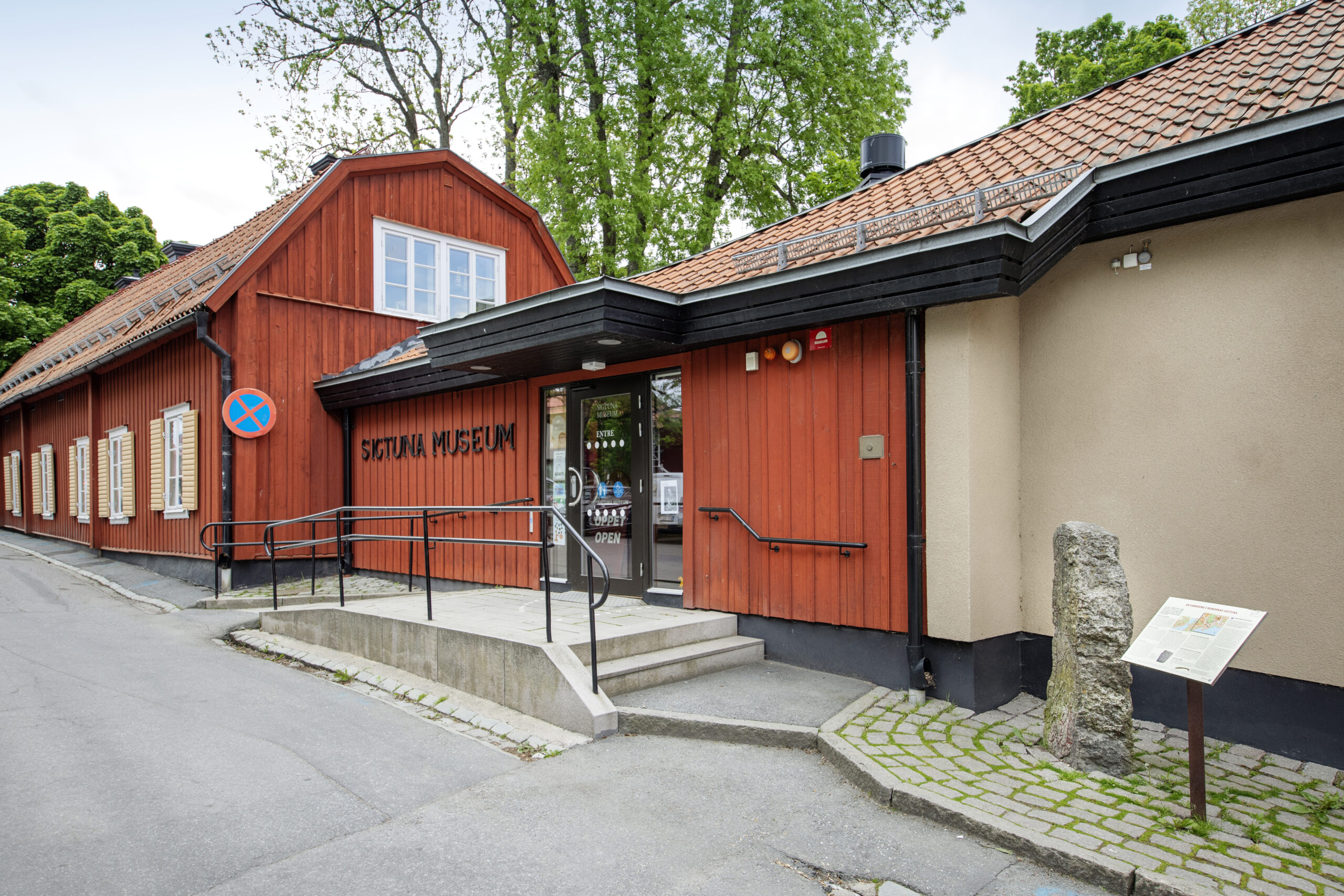 Foto av en äldre röd byggnad sammanbyggd med en modern med putsfasad. På fasadens står: Sigtuna Musem.